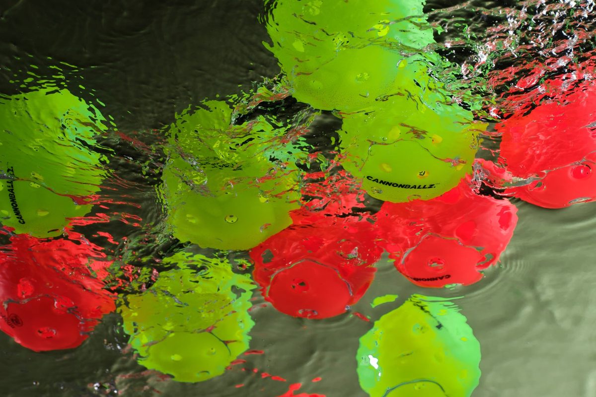 Red and green Cannonballz pickleballs floating in water