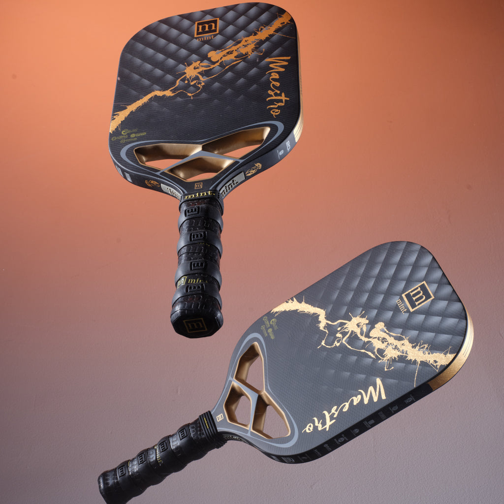 Two Mint Sport Mon Ami black and gold pickleball paddles with an orange and gray gradient background