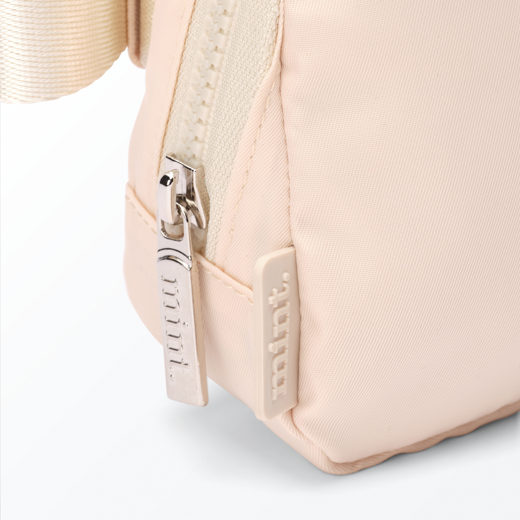 Close-up of a cream-colored Mint Sport belt bag with a zipper on a white background