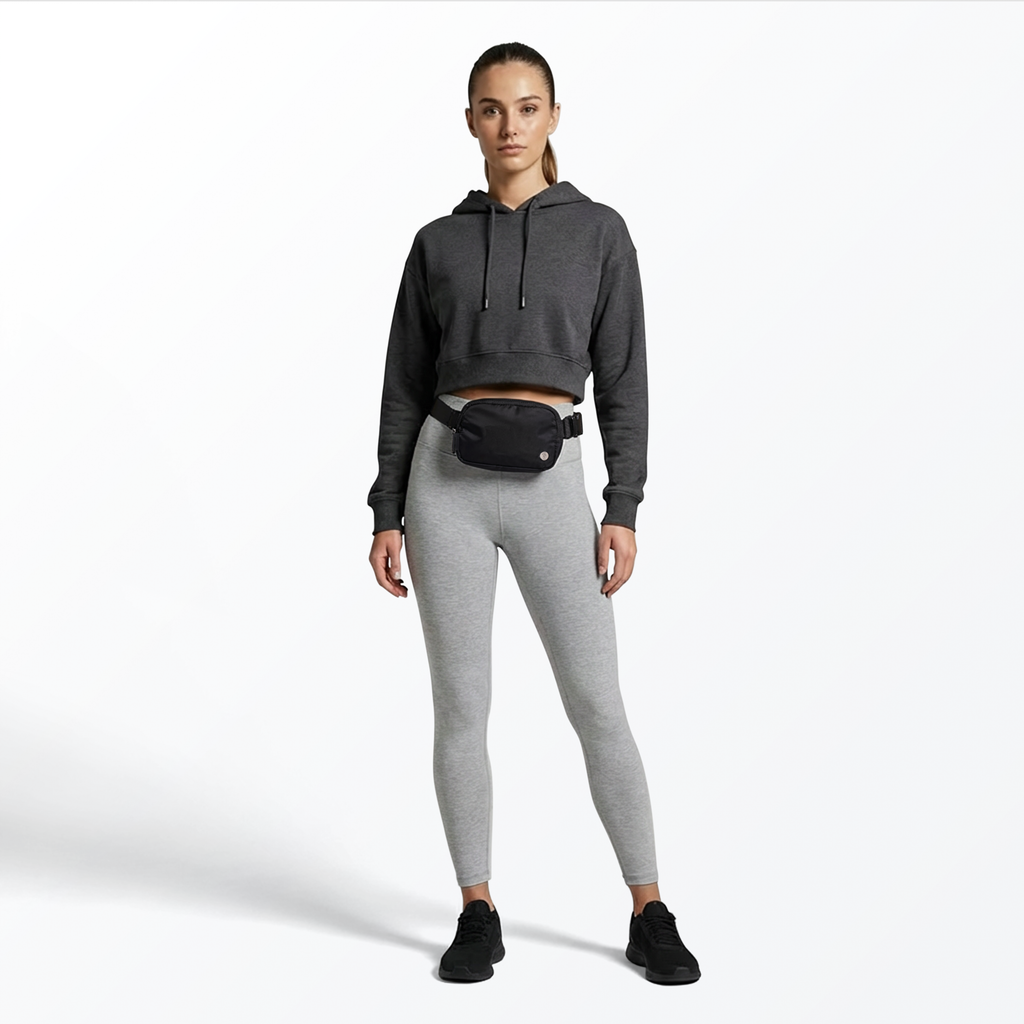 Woman wearing a gray hoodie and leggings with a black Mint Sport belt bag on a white background