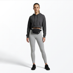 Woman wearing a gray hoodie and leggings with a black Mint Sport belt bag on a white background
