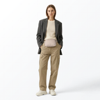 Woman wearing a gray sport jacket, white top, cream-colored Mint Sport belt bag, tan pants, and white shoes on a white background