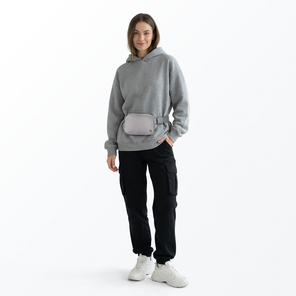 Woman wearing a gray sweatshirt, gray Mint Sport belt bag, black pants, and white shoes on a white background