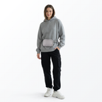 Woman wearing a gray sweatshirt, gray Mint Sport belt bag, black pants, and white shoes on a white background