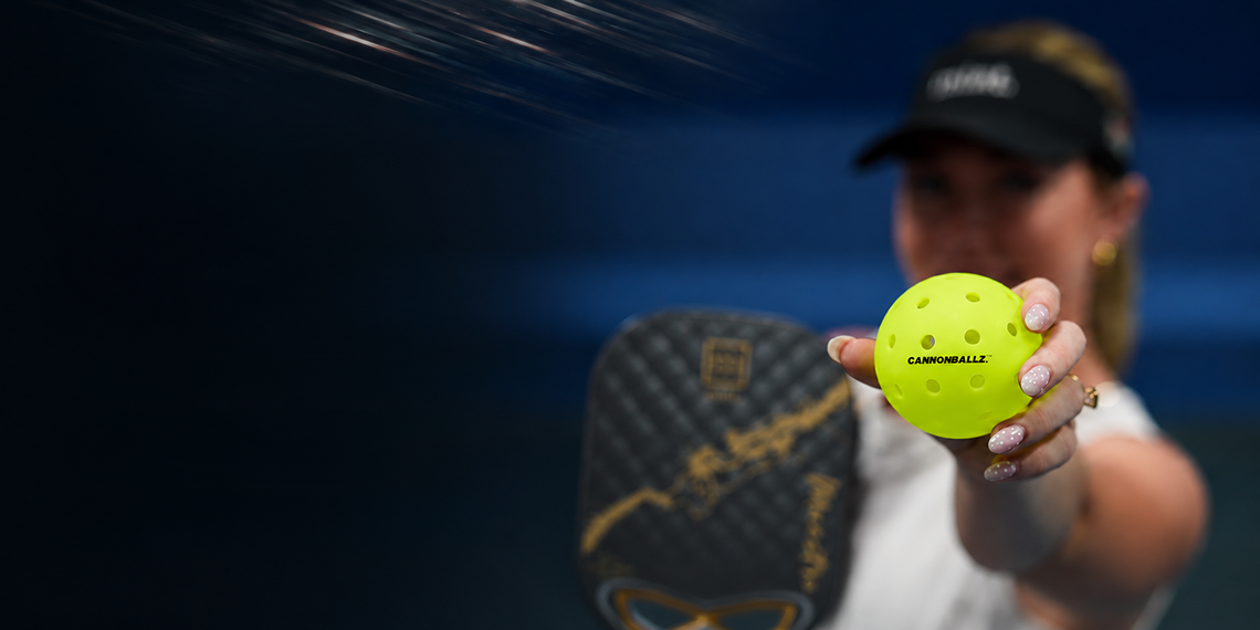A close-up action shot of a player holding a bright yellow pickleball, with the brand name 'CARROSSA' clearly visible on both the paddle and the ball. The player is wearing a black visor and white top, set against a dark blue background with motion blur.