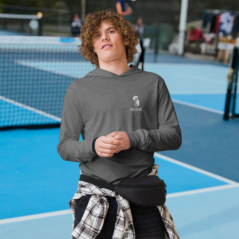 Person wearing a gray hoodie with a logo on a tennis court