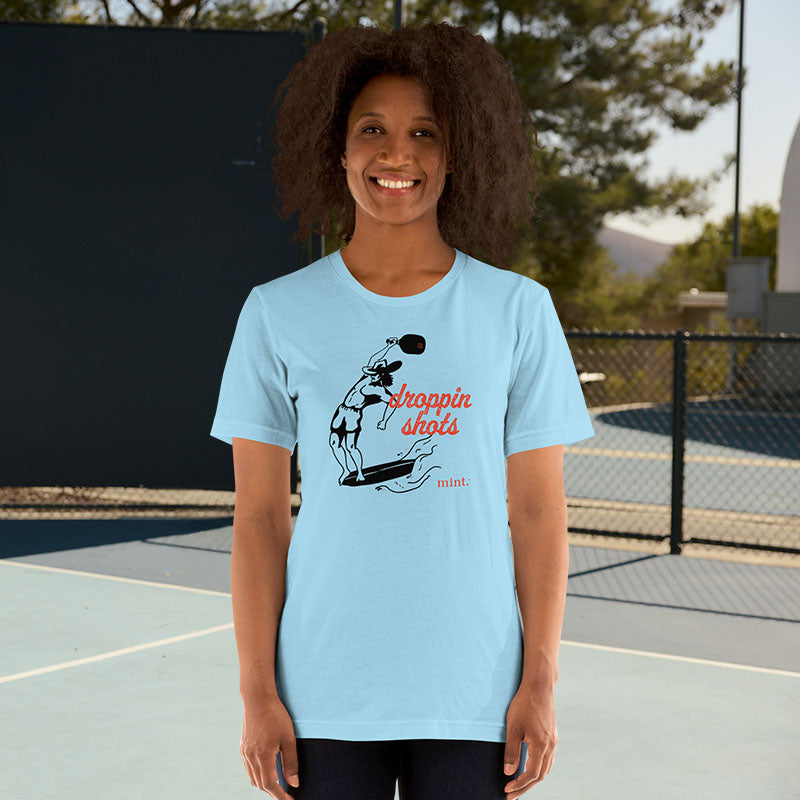 Woman wearing a light blue t-shirt with a graphic design on a tennis court