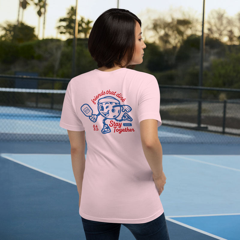 Person wearing a pink t-shirt with a graphic design on the back, standing on a tennis court.