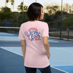 Person wearing a pink t-shirt with a graphic design on the back, standing on a tennis court.