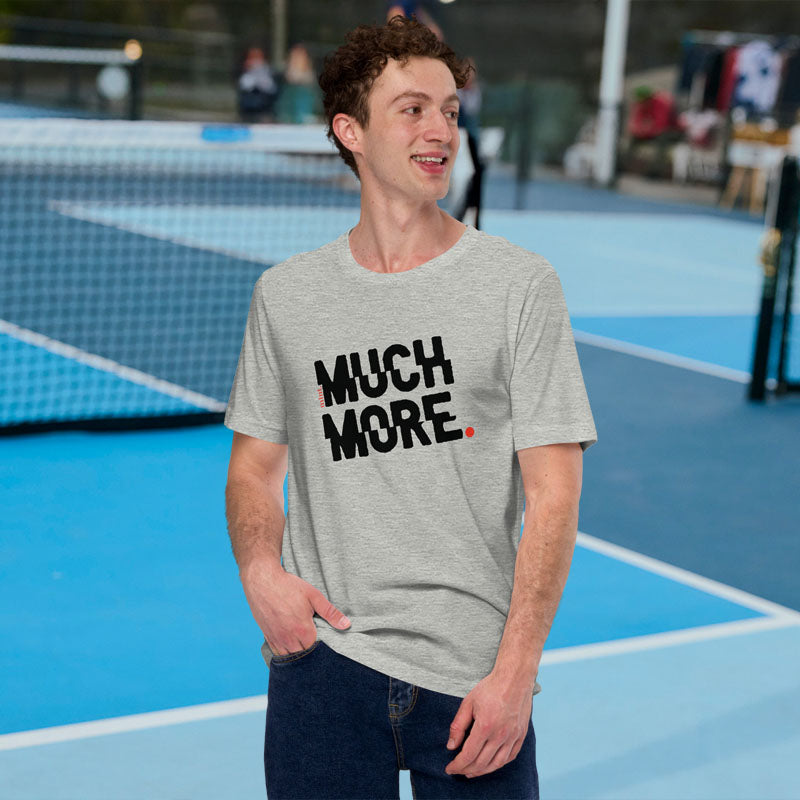 Man wearing a gray t-shirt with 'MUCH MORE' text on a tennis court