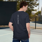 Person wearing a navy blue t-shirt with text on the back, standing on an outdoor court.
