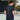 Person wearing a navy blue t-shirt with text on the back, standing on an outdoor court.